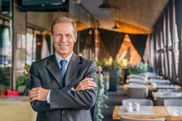 Portrait of a happy successful businessman standing in restaurant with crossed arm