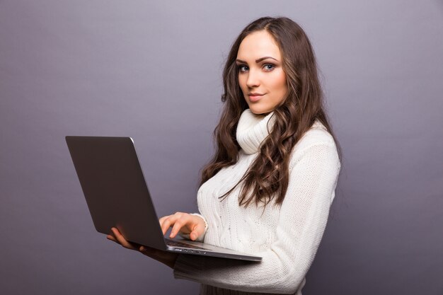 Portrait of happy surprised woman standing with laptop isolated on gray wall