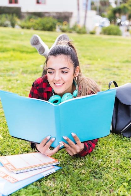 Free photo portrait of a happy teenage girl lying on the lawn reading the book