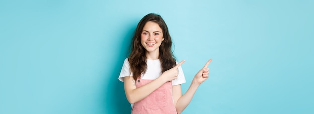 Free photo portrait of happy teenage girl in summer outfit have cute blush and bright make up pointing fingers