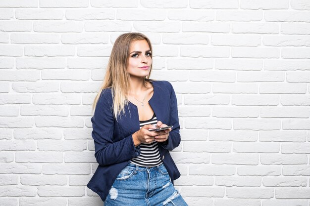 Portrait of happy woman smiling against white brick wall and chatting on mobile phone.