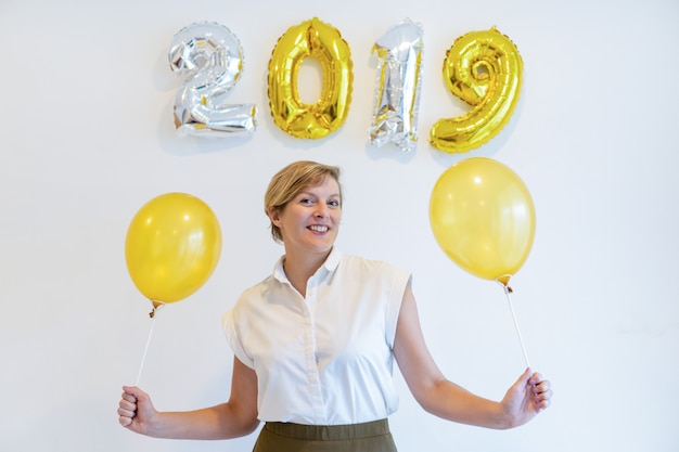 Free photo portrait of happy woman standing with balloons under 2019 sign