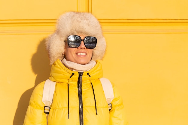 Free Photo portrait of a happy woman with a smile in snow-white zabas in winter against a yellow wall on a sunny day in a warm russian siberian hat