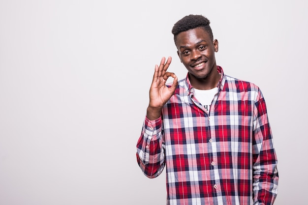 Portrait of a happy young african man in white shirt showing ok gesture isolated