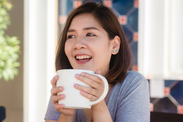 Portrait of happy young asian business woman with mug in hands drinking coffee in the morning