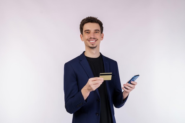 Portrait of happy young businessman standing using mobile cell phone and holding credit bank card isolated on white color background studio