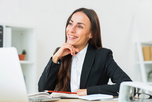 Portrait of happy young businesswoman sitting at workplace daydreaming