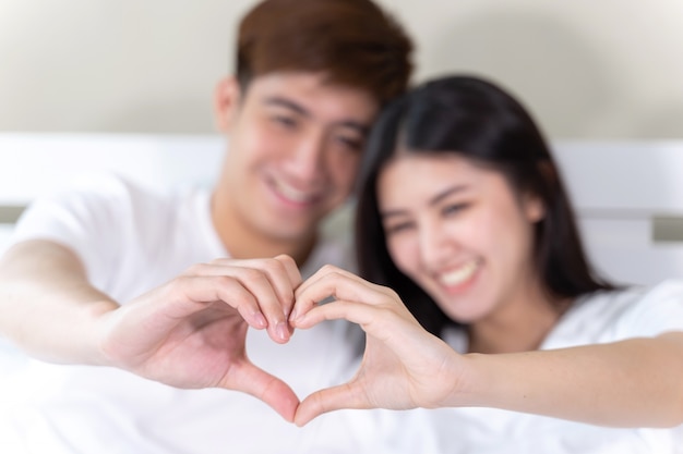  Portrait happy young couple sitting and smiling on bed and hand make heart shape together