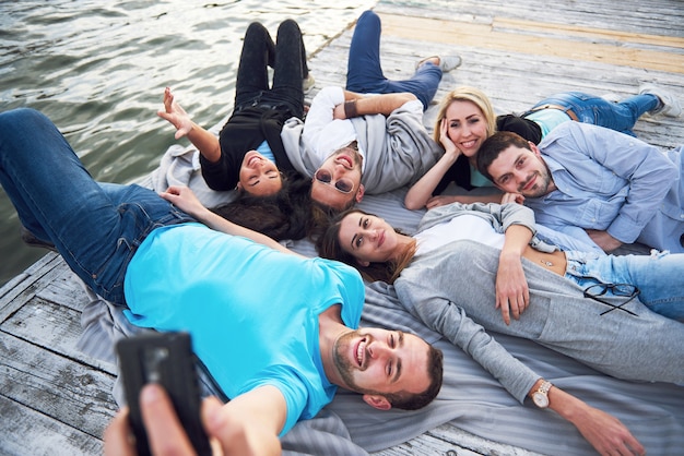 Portrait of happy young friends on the pier at the lake. While enjoying the day and doing selfie.