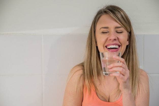 Free photo portrait of happy young woman drinking water against kitchen background. healthy lifestyle. healthcare. drinks. health, beauty, diet concept. healthy eating.