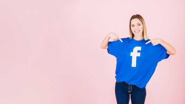 Free Photo portrait of a happy young woman pointing at her t-shirt with facebook icon