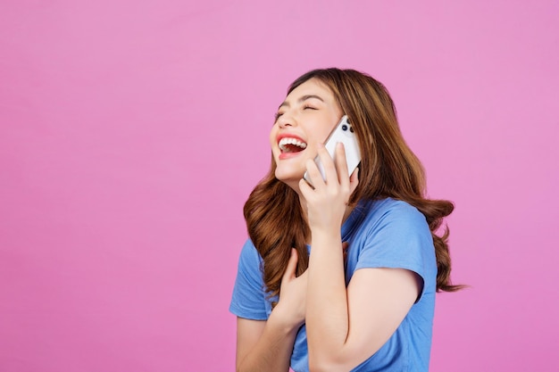 Portrait of happy young woman wearing casual tshirt talking on mobile phone isolated over pink background