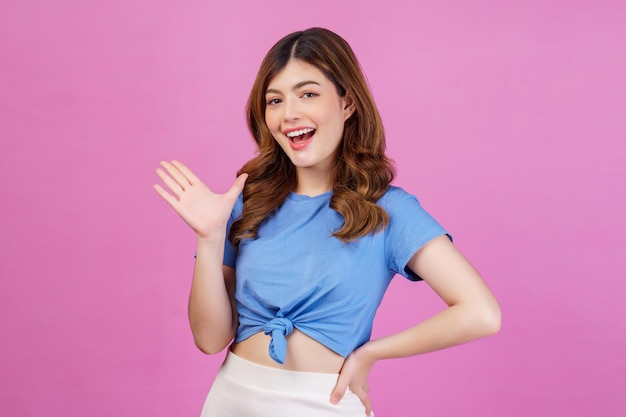 Portrait of happy young woman wearing casual tshirt waving hands isolated over pink background