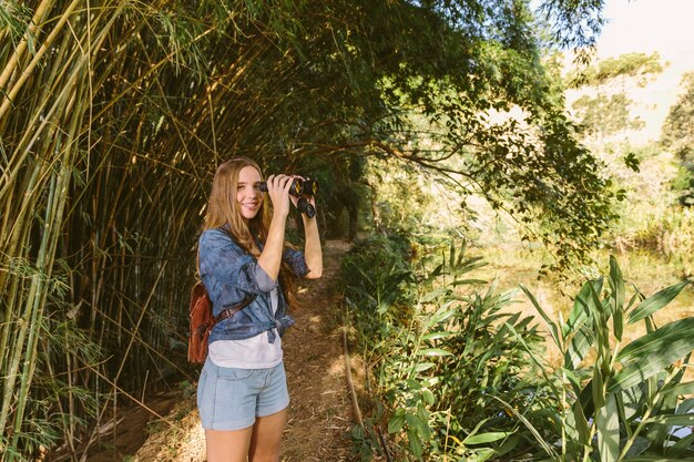 Portrait of a happy young woman with binoculars standing in forest