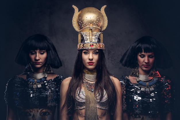 Portrait of haughty Egyptian queen in an ancient pharaoh costume with two concubines. Isolated on a dark background.