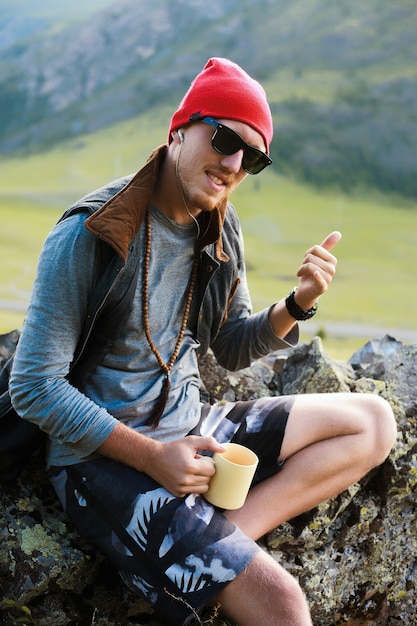 Free photo portrait of hipster man traveling at mountains,wear red hat and hipster clothes,make pictures