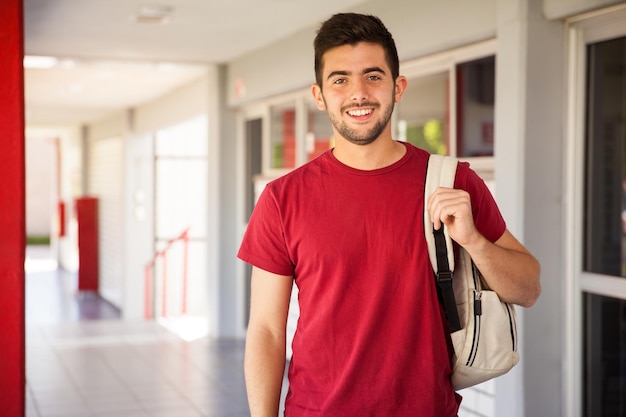 Portrait of a Hispanic college student carrying a backpack and standing in a school hallway