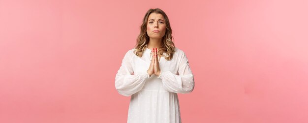 Portrait of hopeful clingy girlfriend blond girl begging for favour in white dress over pink background sobbing make cute eyes pleading or praying say please want something badly