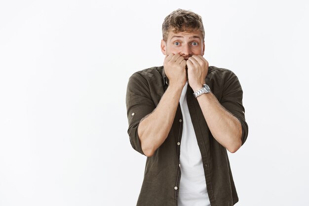 Portrait of intese scared cute guy in stupor widen eyes biting fingernails and looking worried at front as troubled and concerned, feeling guilty making mistake over gray wall