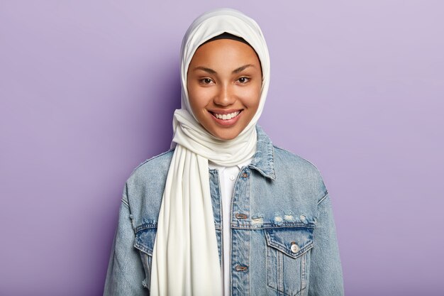 Portrait of joyful good looking woman has Islamic views, smiles gently at camera