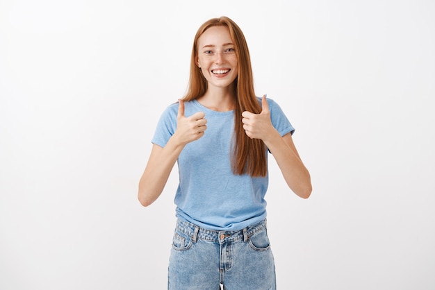 Free photo portrait of joyful pleased good-looking redhead female with freckles showing thumbs up and smiling supportive and cheering giving positive answer