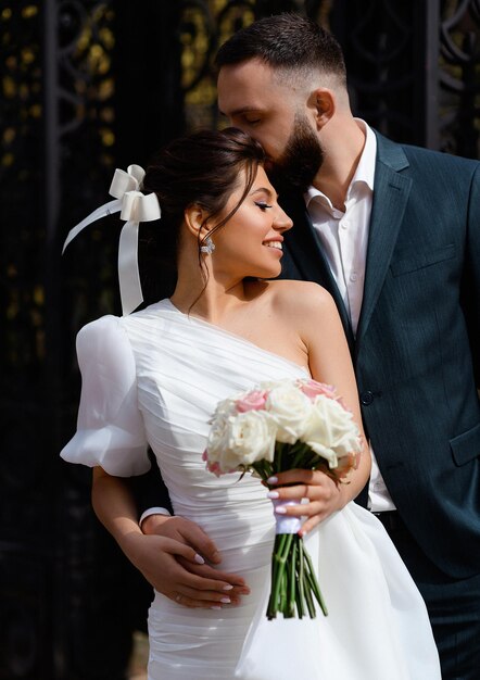 Portrait of joyful woman with hairstyle wearing in oneshoulder dress and other side bare holding bouquet of white and pink roses smiling