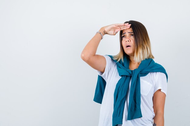 Portrait of lady with tied sweater looking far away with hand over head in white t-shirt and looking focused front view