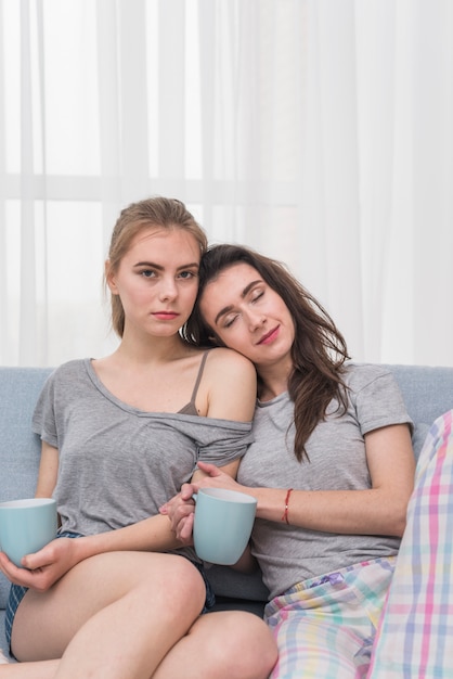 Portrait of a lesbian young couple sitting on sofa holding blue cup of coffee