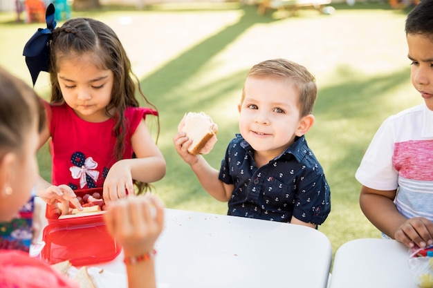 Portrait of a little boy eating a sandwich and smiling during his lunch break at kindergarten