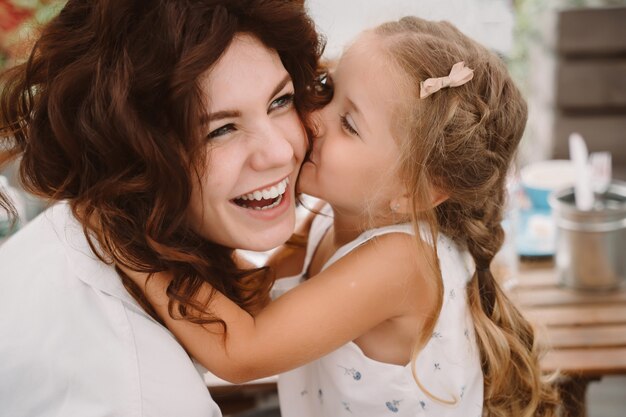 Portrait of little daughter kissing her beautiful happy mother outdoors