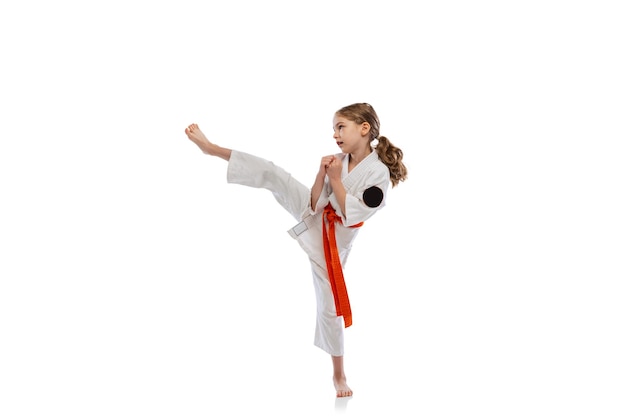 Portrait of little girl, child in kimono training karate isolated on white. Fight