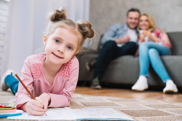 Portrait of a little girl drawing on book with her parents in blurred background