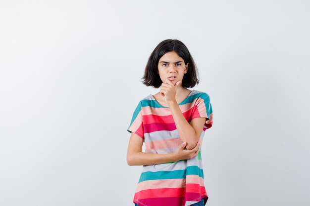 Portrait of little girl keeping hand on chin in t-shirt and looking upset front view