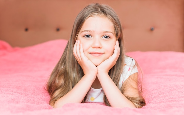 Free Photo portrait of a little girl lying on pink blanket sheet on bed