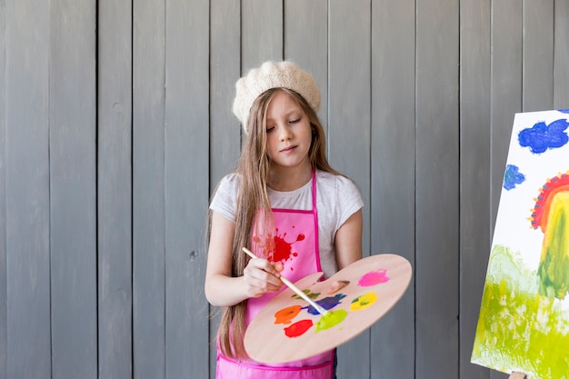 Free Photo portrait of a little girl standing against grey wall painting with brush against gray wall