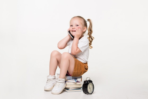 Free photo portrait of a little girl talk phone sitting on a stack of books.