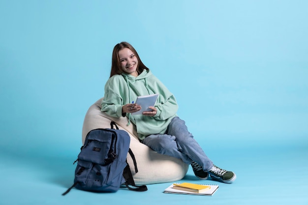 Free photo portrait of lively young girl sitting on beanbag reviewing school notes