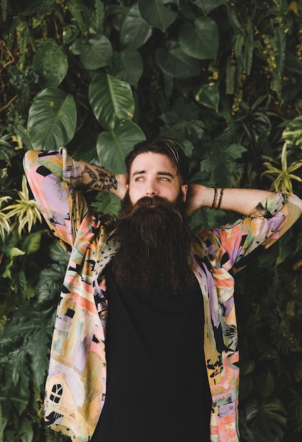 Free photo portrait of long bearded young man standing in front of green leaves