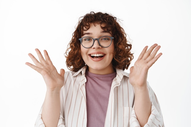 Portrait of looks surprised and relieved, clap hands and gasp amazed, smiling happy, cheering from good news, standing on white