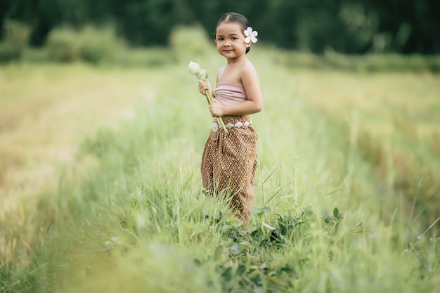 Portrait of lovely girls in Thai traditional dress and put white flower on her ear,  Standing and hold two lotus in hand on rice field, She smile with happiness, copy space