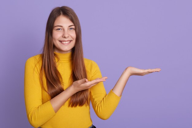 Portrait of magnificent lovely adorable girl in casual yellow shirt, pointing aside with two palms