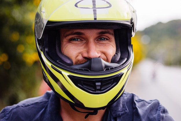 Portrait of male biker in yellow helmet on motorbike on side of busy road in Thailand