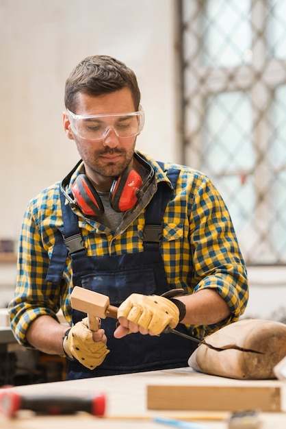 Free photo portrait of a male carpenter making wooden shape with chisel