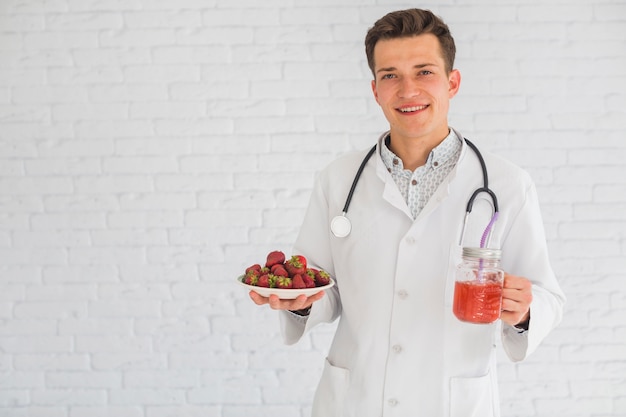 Portrait of male doctor holding strawberry fruits and smoothie