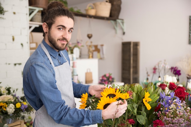 Free photo portrait of a male florist holding arranging the flower bouquet looking to camera