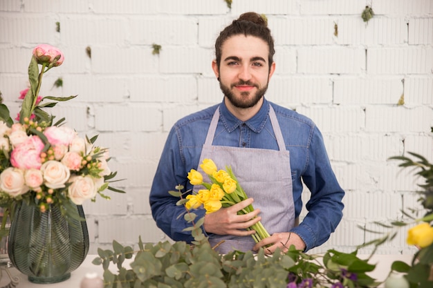 Free photo portrait of a male florist holding yellow tulips in hand against white wall