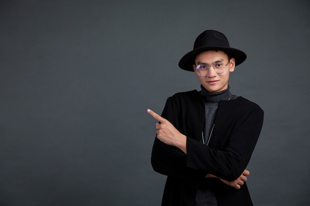 Portrait of male model pointing finger and smiling on dark  wall