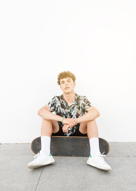 Free photo portrait of male skater wearing white shoes sitting against white wall