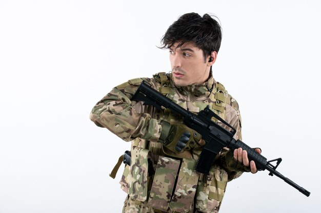 Portrait of male soldier in military uniform with rifle white wall