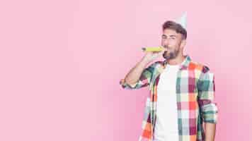 Free photo portrait of a man blowing party horn on pink background